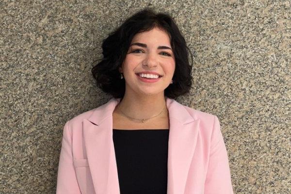 Grace VanEtten '27 in black top and pink blazer, stands against a stone wall.